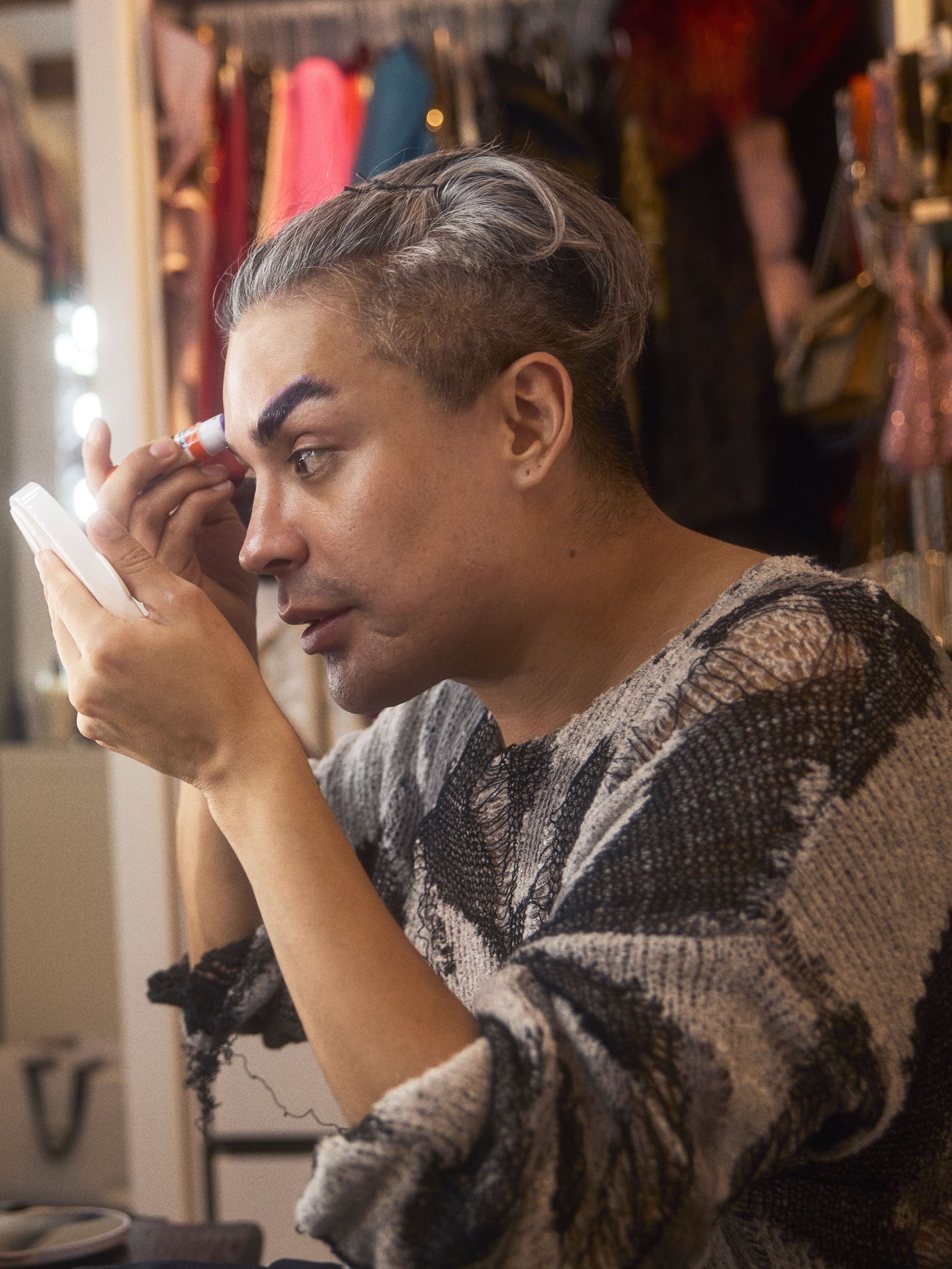 Mężczyzna malujący się przy małym lusterku w garderobie.