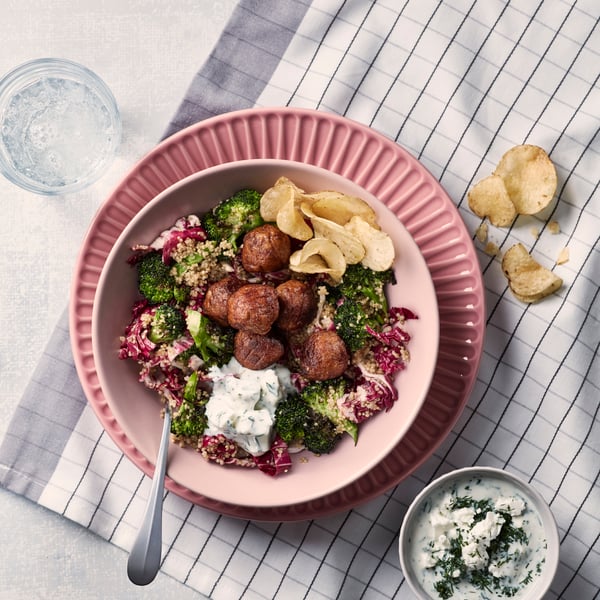 Plant balls with quinoa salad in a pink bowl on a pink plate, which stands on a white and gray checked tea towel.
