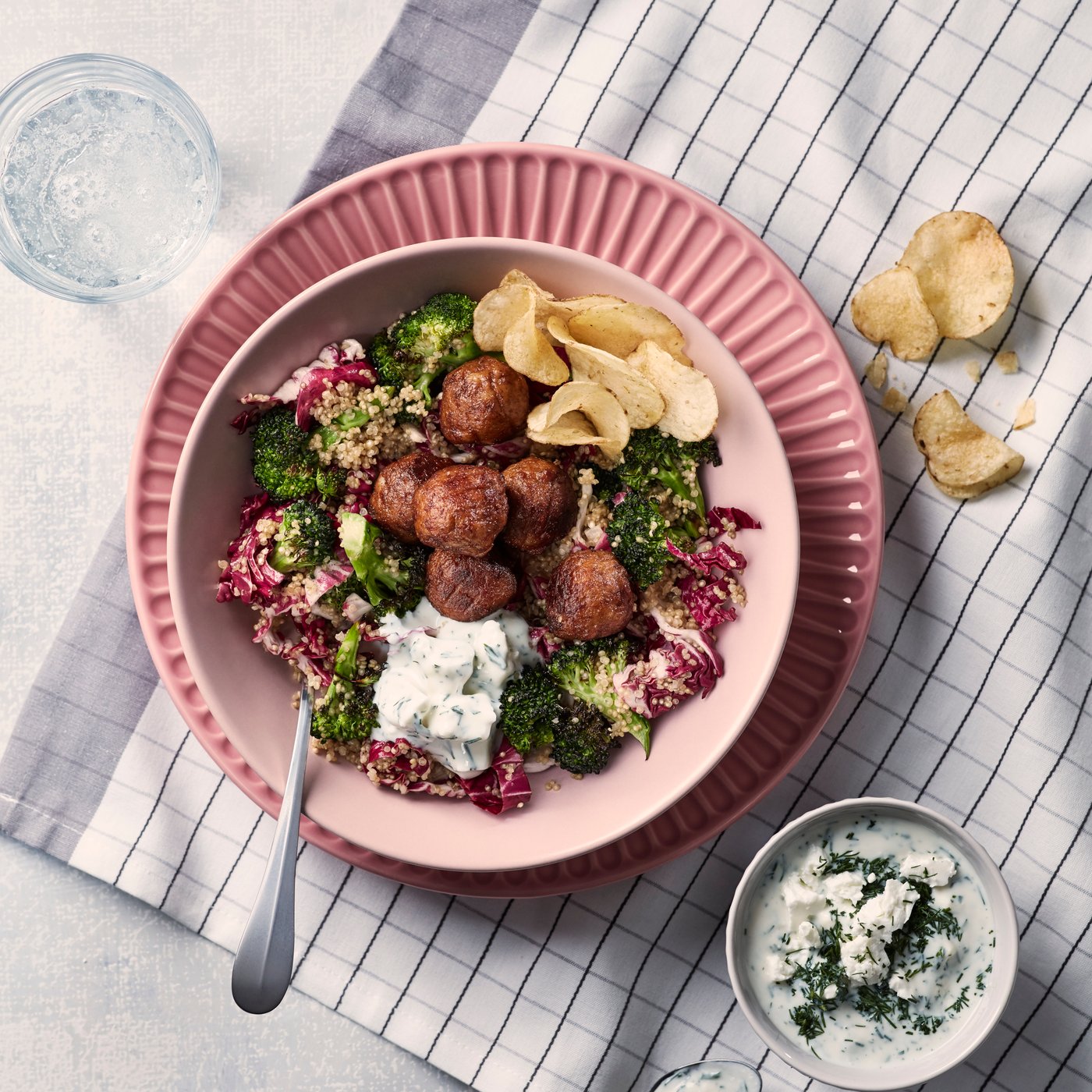Plant balls with quinoa salad in a pink bowl on a pink plate, which stands on a white and grey checked tea towel.