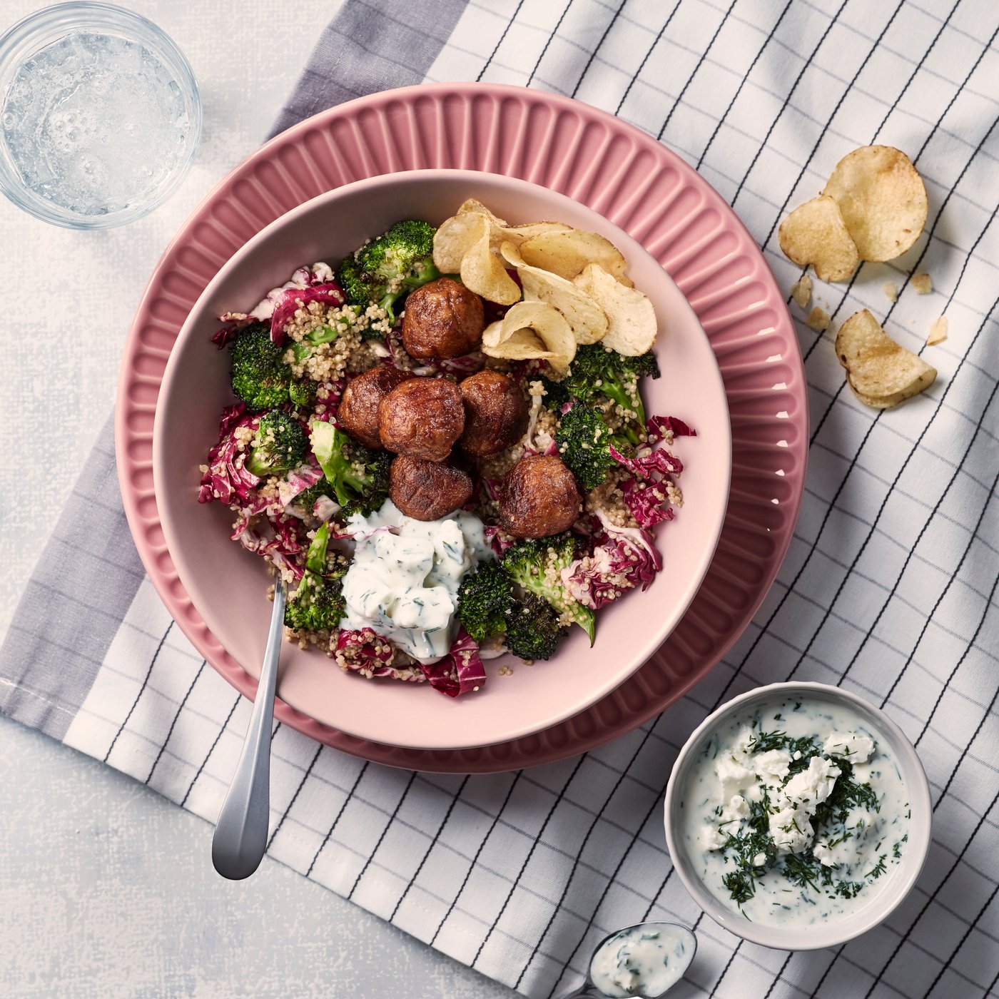 Sur une serviette à carreau, boulettes végétales et salade de quinoa dans un bol rose posé sur une assiette rose.