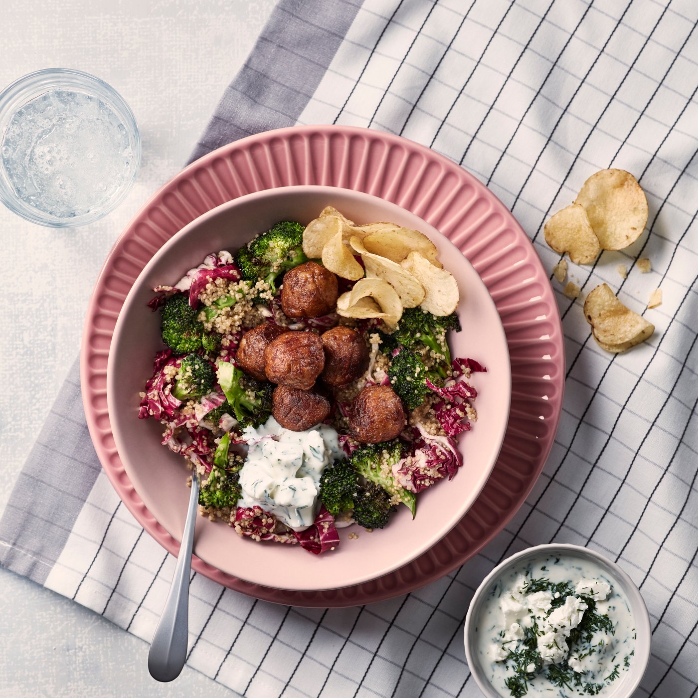 Plant balls with quinoa salad in a pink bowl on a pink plate, which stands on a white and gray checked tea towel.