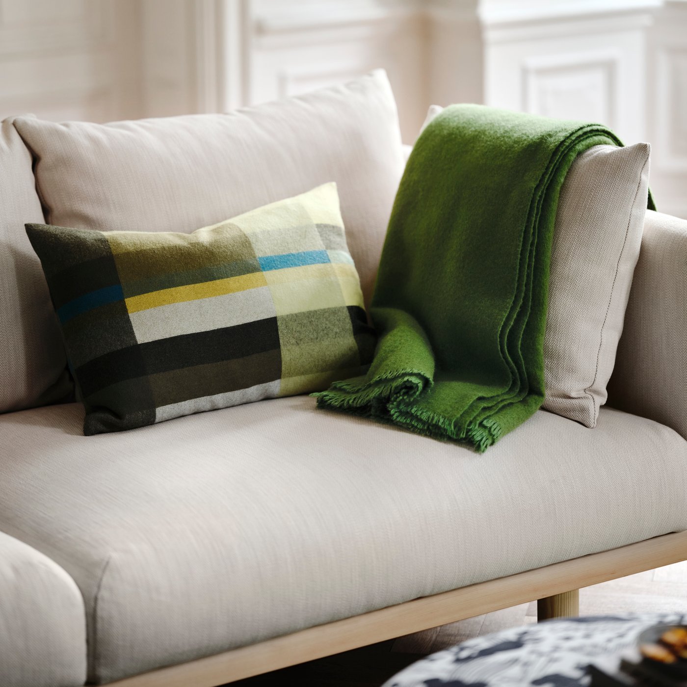 A bright living room with a beige STOCKHOLM 2025 three-seat sofa, featuring colourful cushions and a soft green throw.