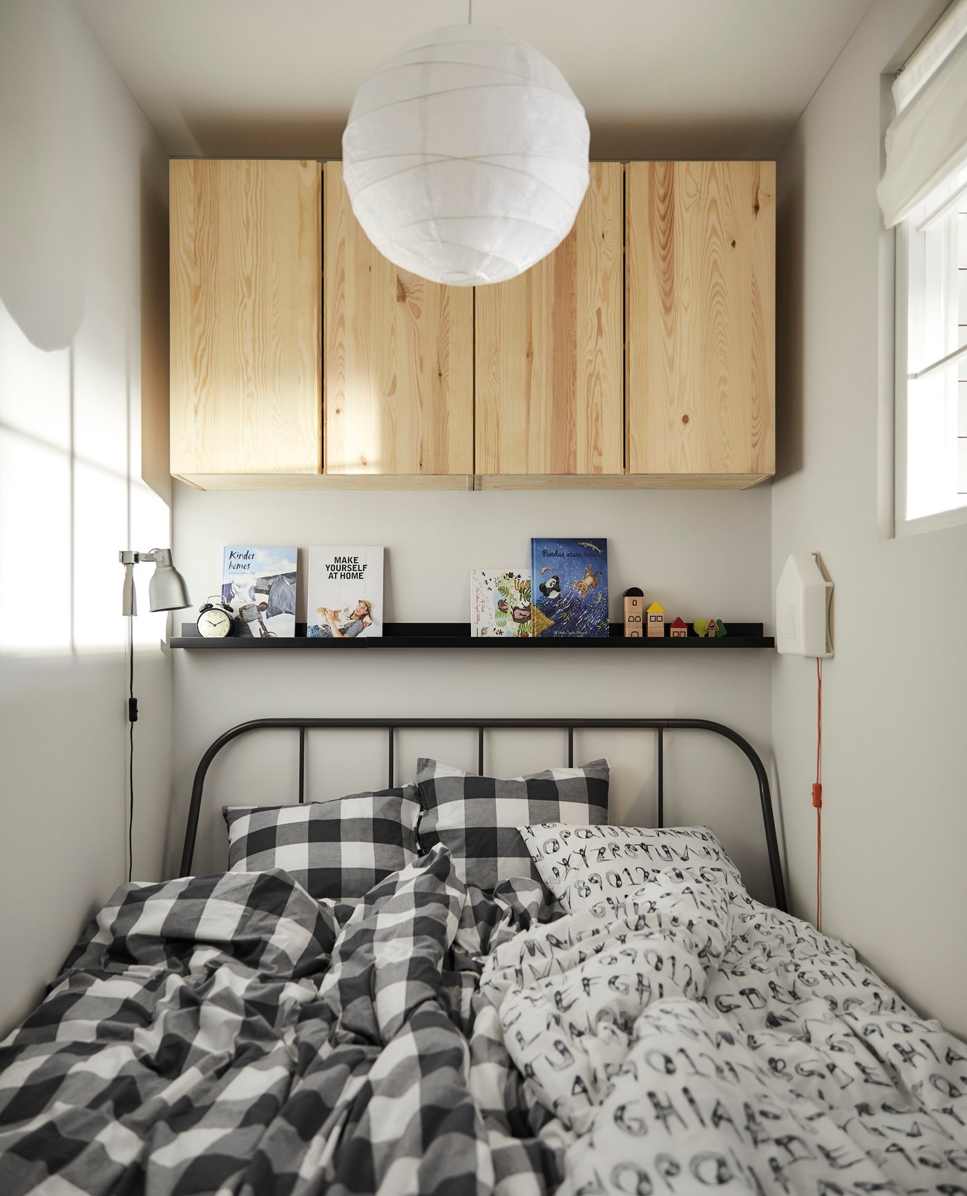 Ein KOPARDAL Bettgestell in Grau mit zwei Bettdecken. Auf der Bilderleiste darüber sind Bücher zu sehen, Holzschränke an der Wand.