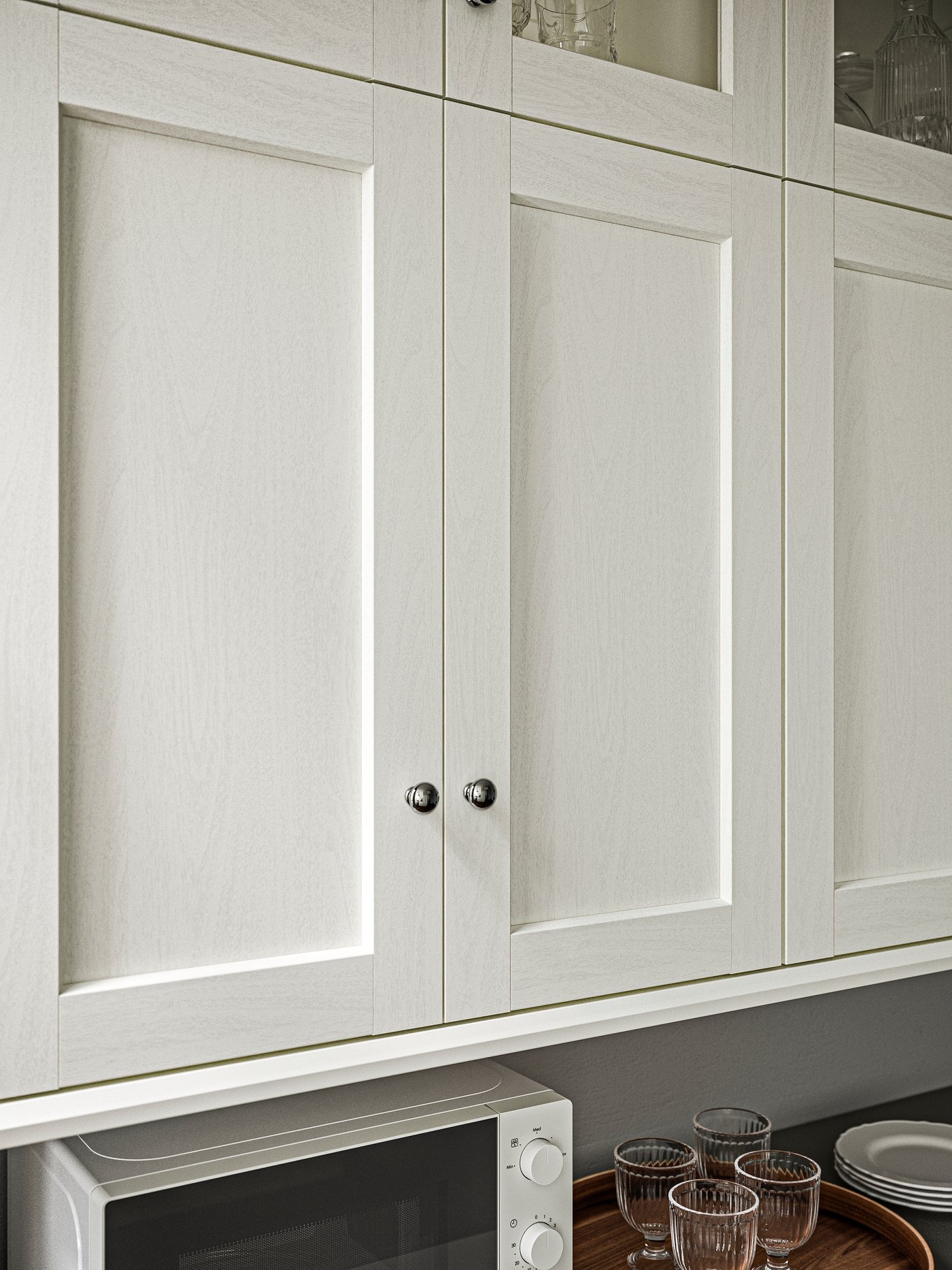 A SEKTION kitchen wall cabinet with ENKÖPING white kitchen front doors above a worktop with a microwave oven and glasses.