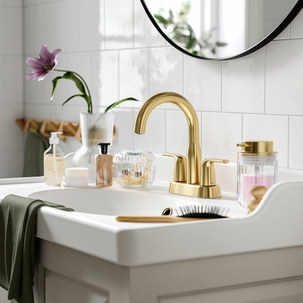 A brass-color MACKSJÖN bathroom faucet with a white sink.