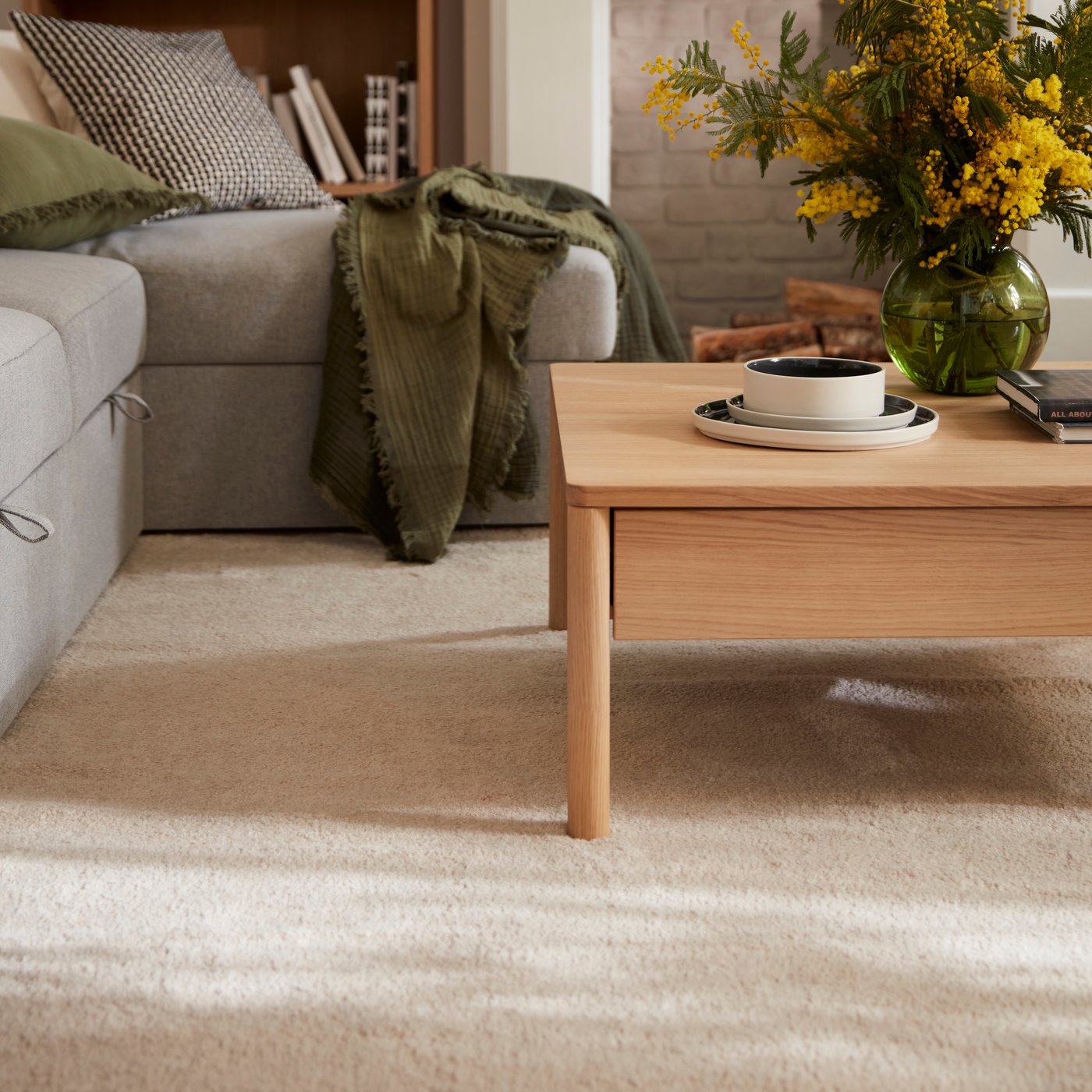 En STOENSE matta vid en grå soffa och ett soffbord i trä.