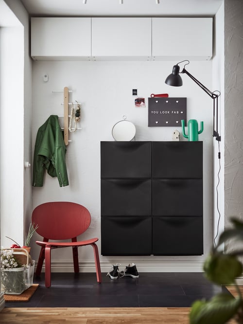 Hol cu mai multe dulapuri negre TRONES amplasate între un fotoliu FRÖSET și o lampă de lucru TERTIAL.