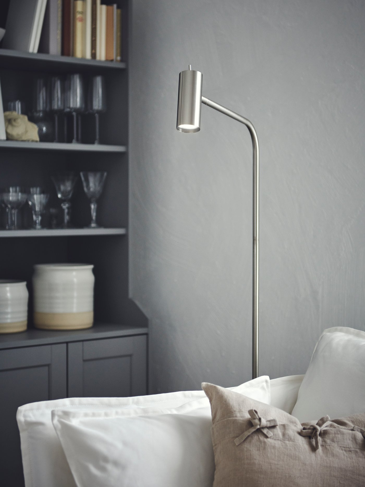A corner with a lit nickel-plated VIRRMO floor lamp standing between a white BACKSÄLEN armchair and a grey HAUGA cabinet.