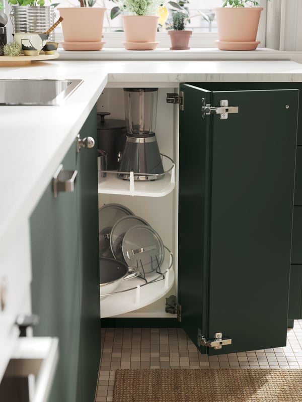 A cabinet with deep green kitchen fronts and doors open, showing an UTRUSTA corner base cabinet carousel with various items.
