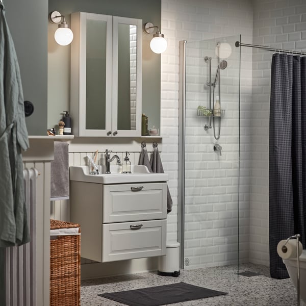 A small bathroom with a white mirror cabinet, a grey wash-stand, a dark grey bath mat and a shower curtain in anthracite.
