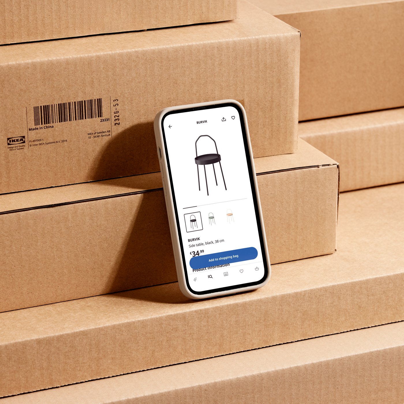 Auf einem Handy ist die IKEA App geöffnet. Das Handy lehnt an mehreren IKEA Paketen.