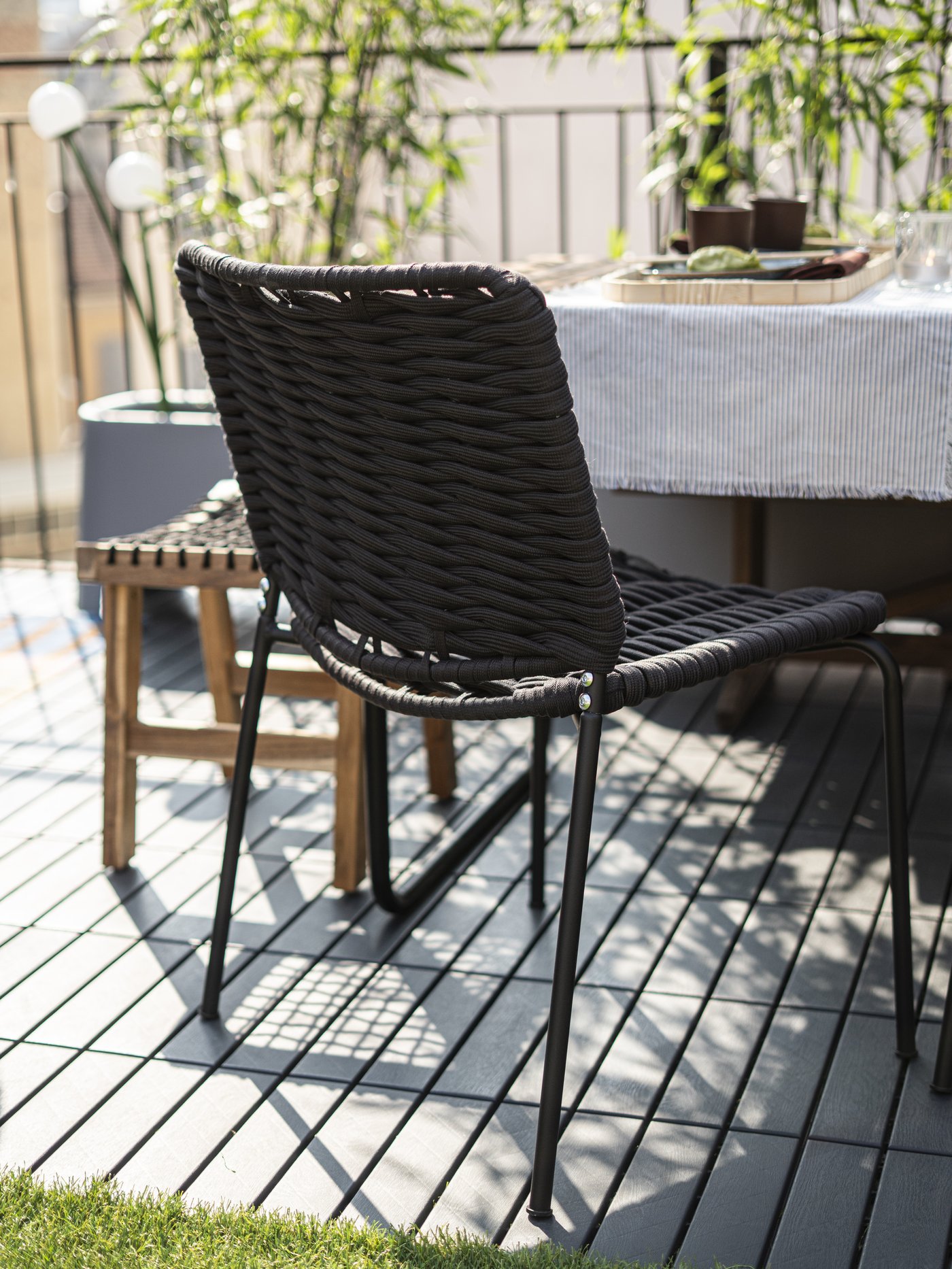 Spazio esterno con in primo piano la sedia TEGELÖN intrecciata nero/grigio scuro, adatta sia per gli spazi interni sia per l’esterno.