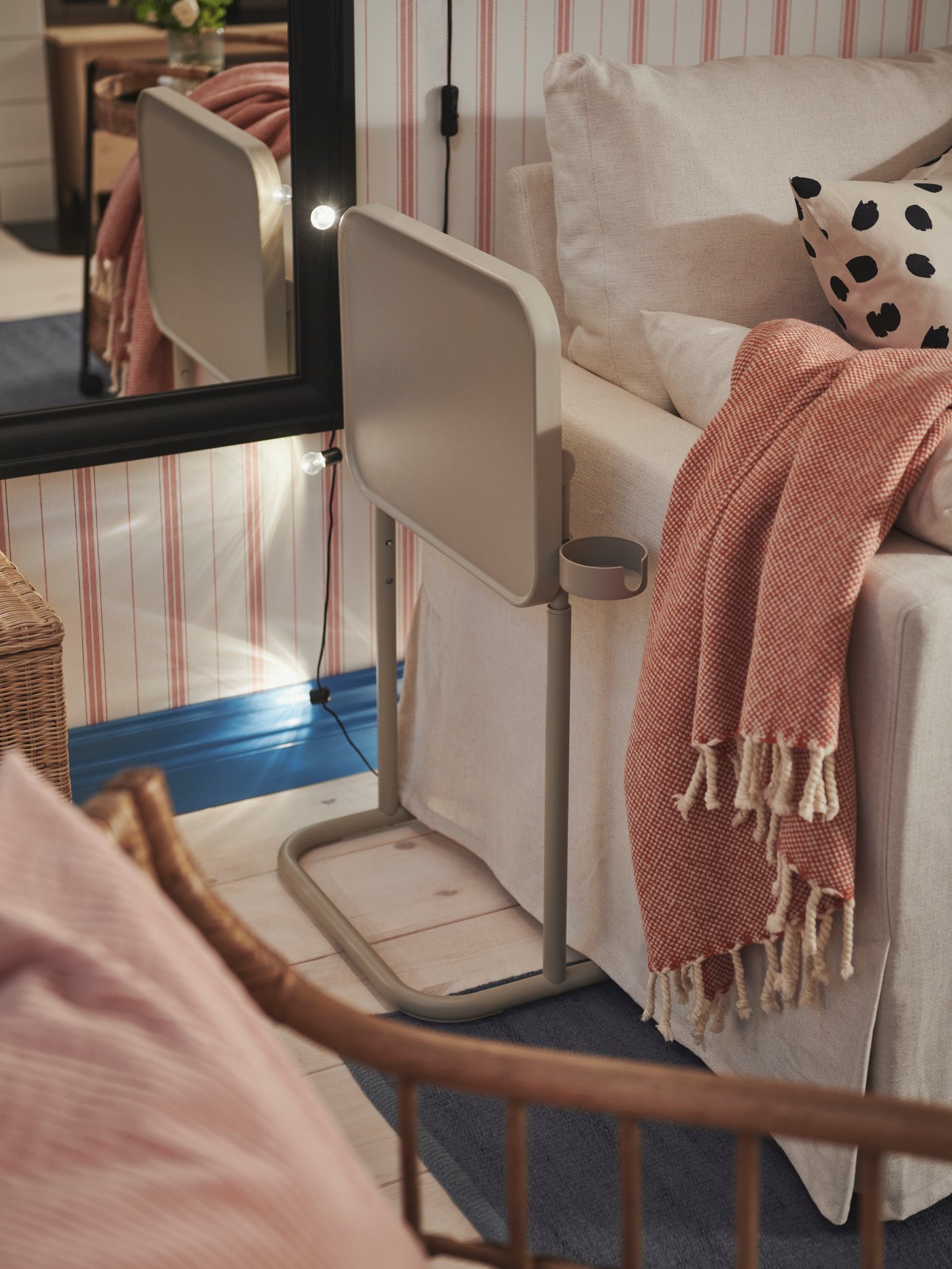 حامل لابتوب BJÖRKÅSEN مطوي بجوار كنبة-سرير HYLTARP عليها غطاء ULLTISTEL على أحد جانبيها.