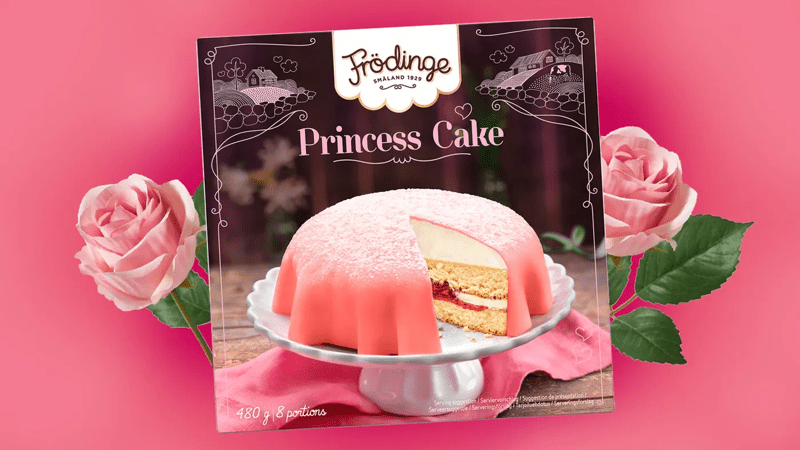 Kuvan keskellä on Frödinge-prinsessakakku ja sen ympärillä kaksi ruusua.