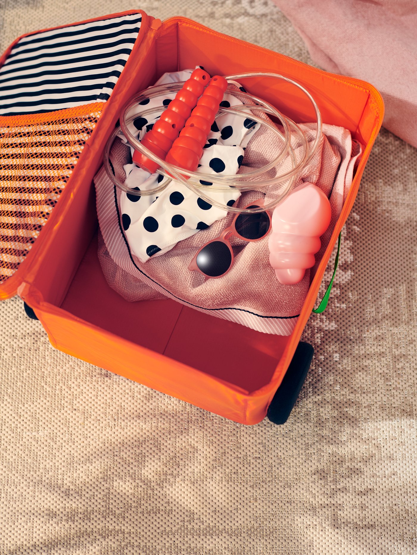 A skipping rope, sunglasses and other beach gear are packed into an orange storage box that looks like a rolling suitcase.