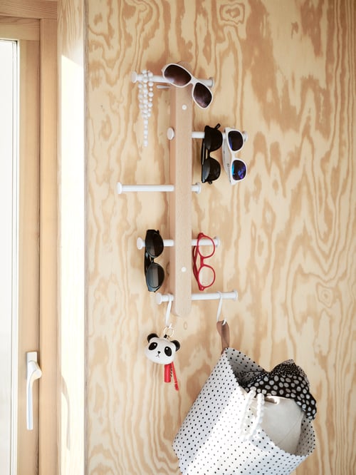 Hallway with wooden vertical hook rack placed on the wall, next to a door, with pairs of sunglasses, keys, and bag on hooks.