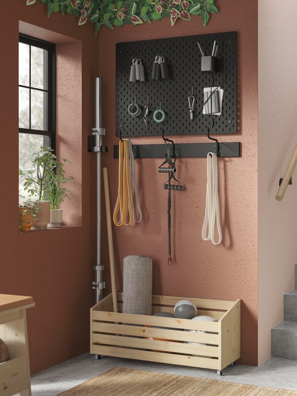A corner with plants in a window and gym accessories on a pegboard, a PINNIG hook rack, and an IVAR storage unit on wheels.