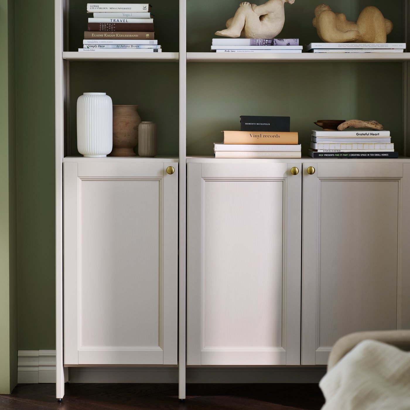 A living room with a beige GULDDRAGARE storage combination featuring doors and shelves, set against a green wall.