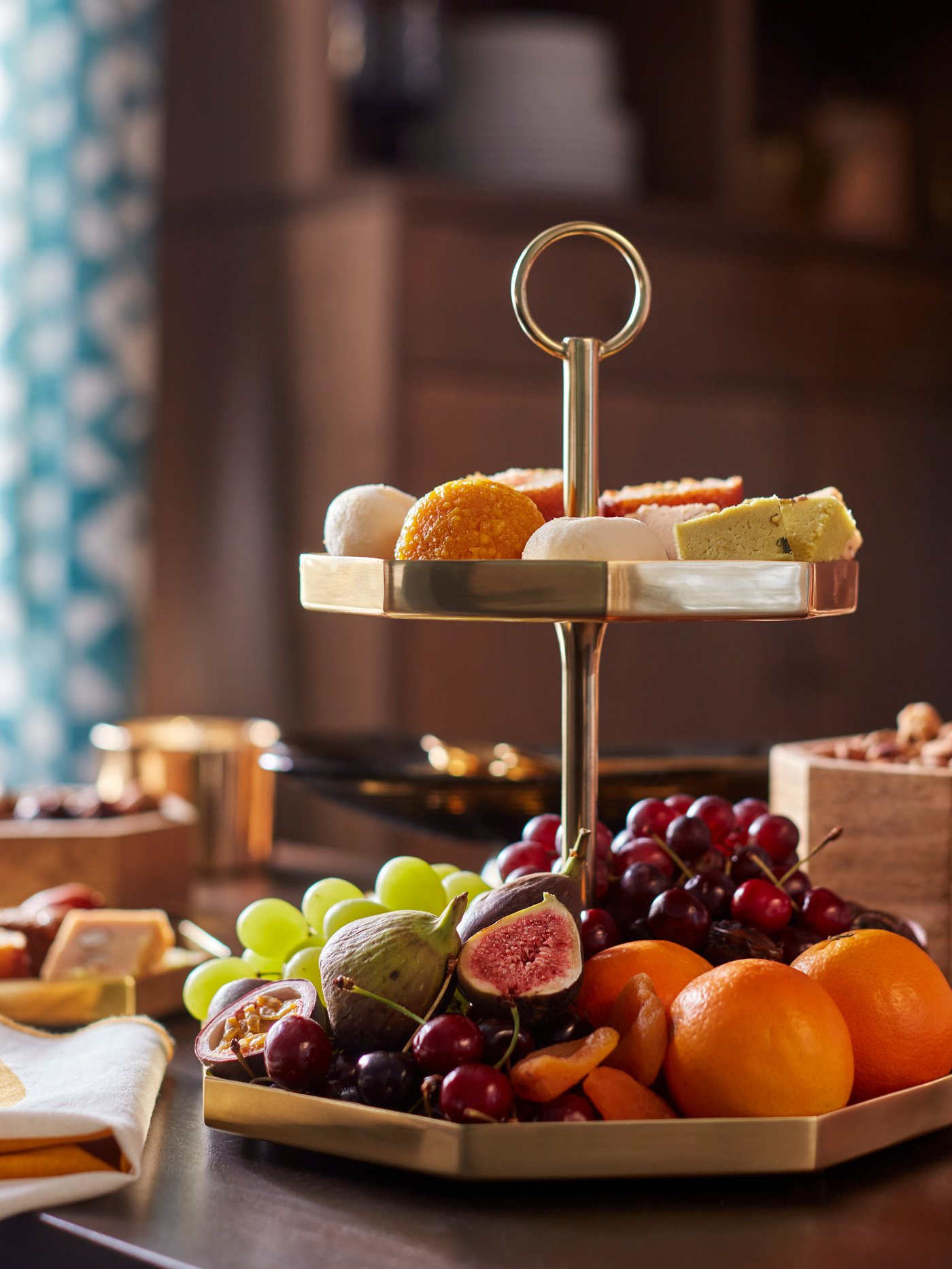 A two-tier GOKVÄLLÅ serving stand filled with fresh fruit and more. There is a GOKVÄLLÅ napkin next to the serving stand.
