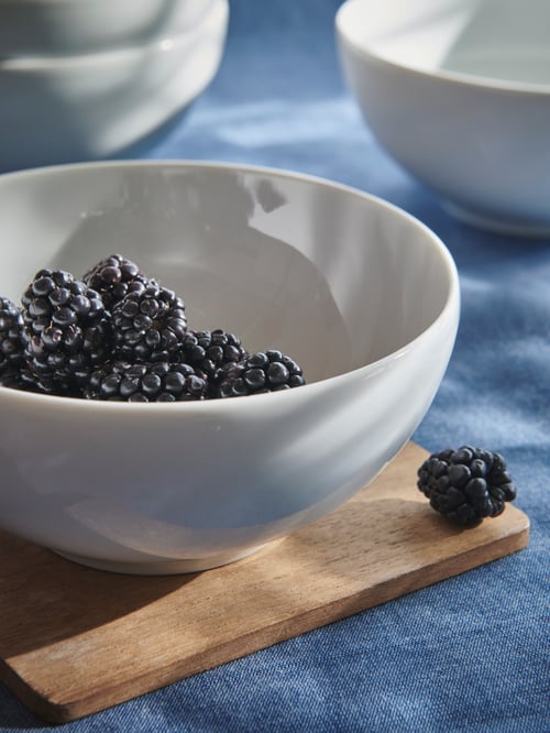 Close-up on dining table with simple white bowl made of Feldspar porcelain, holding berries, on a wooden worktop.