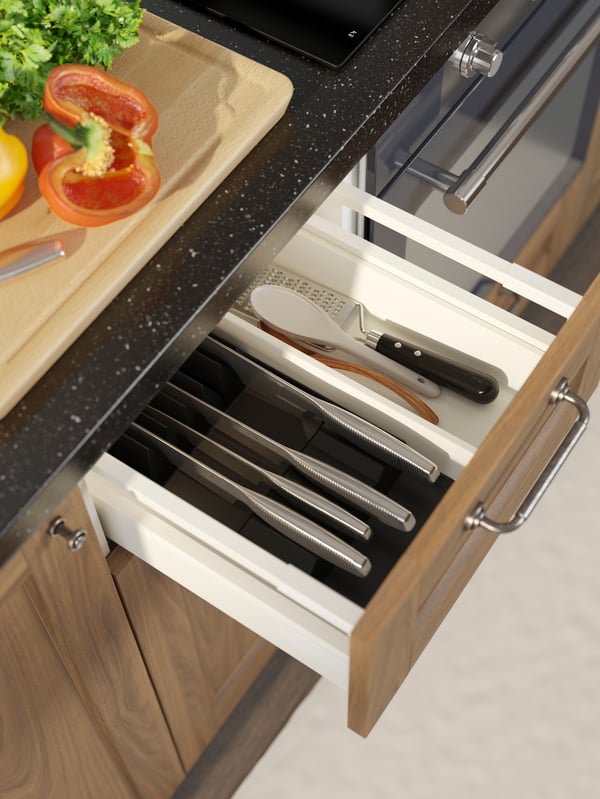 An open kitchen drawer containing an UPPDATERA tray with knife rack that’s filled with knives and other kitchen utensils.