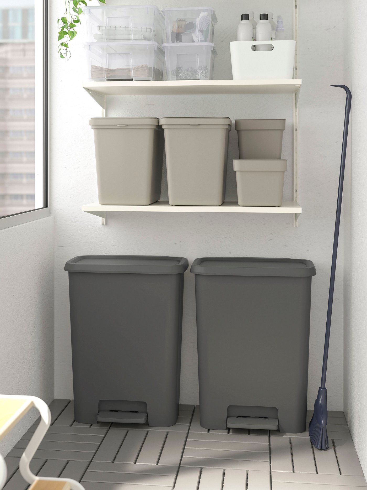 El rincón de un lavadero con dos basureros KNÖCKLA con pedal grises y sobre ellos repisas con otras cajas plásticas.