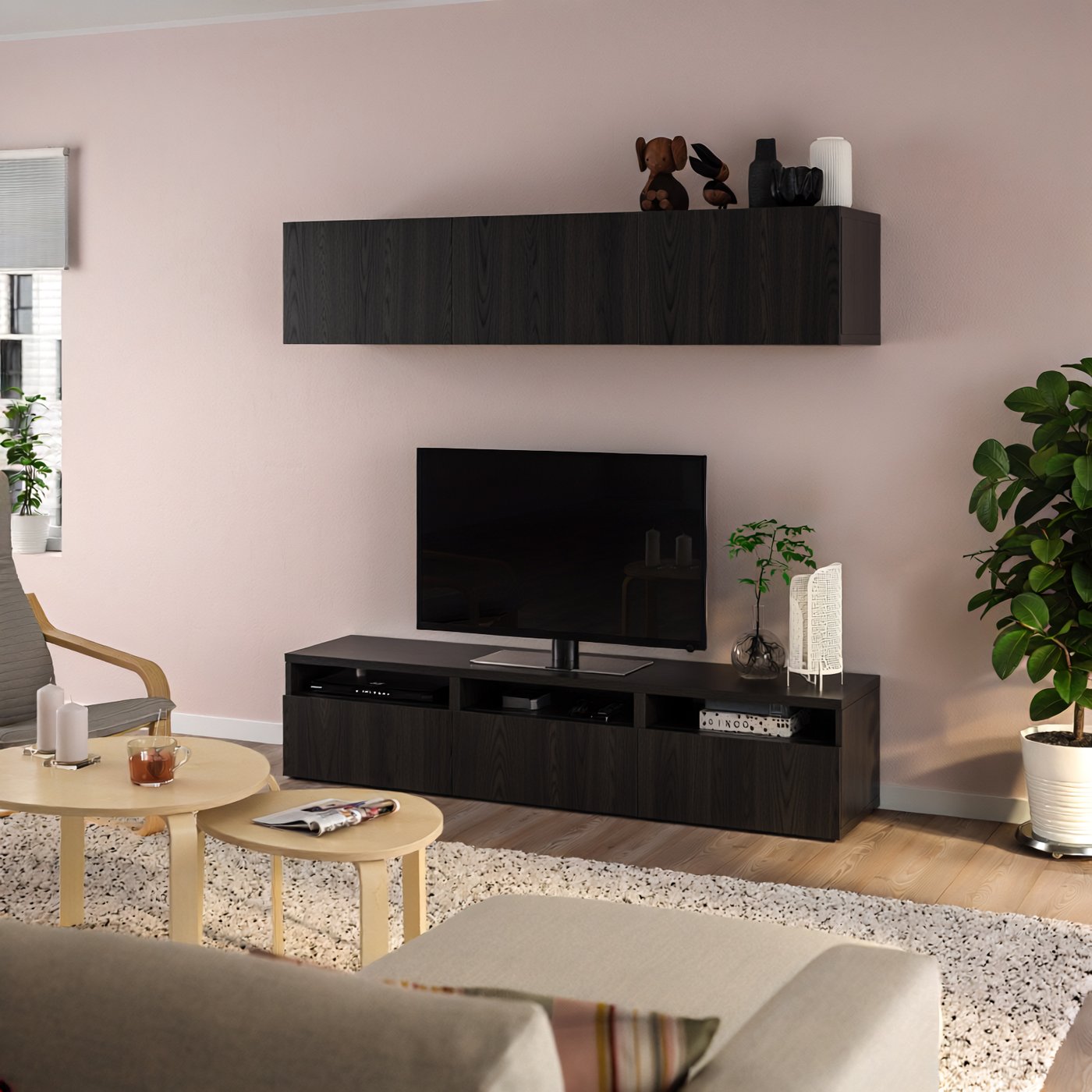 Composizione soggiorno con mobile TV BESTÅ marrone nero, contro una parete rosa chiaro in un soggiorno con divano beige e tavolini da caffè.