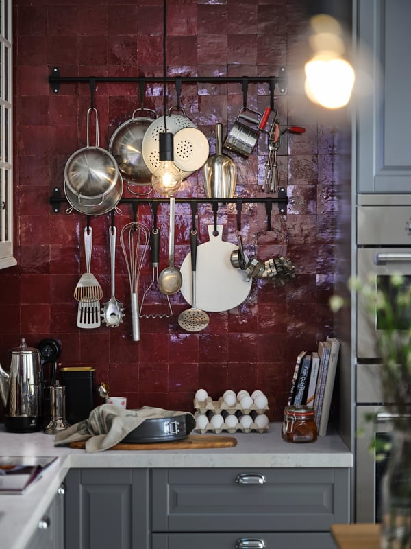 Multiple utensils hanging from black HULTARP rails in a red-tiled kitchen with a white marble-effect worktop and grey fronts.