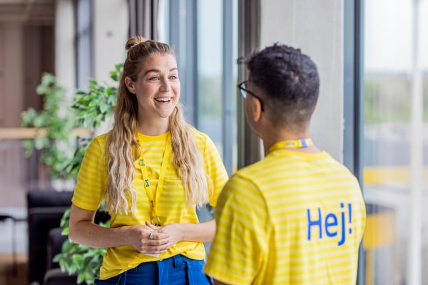 Deux collaborateurs IKEA, l'une en face de l'autre en train de discuter, les deux ont un T-shirts avec le message « Hej! » (bonjour en suédois)