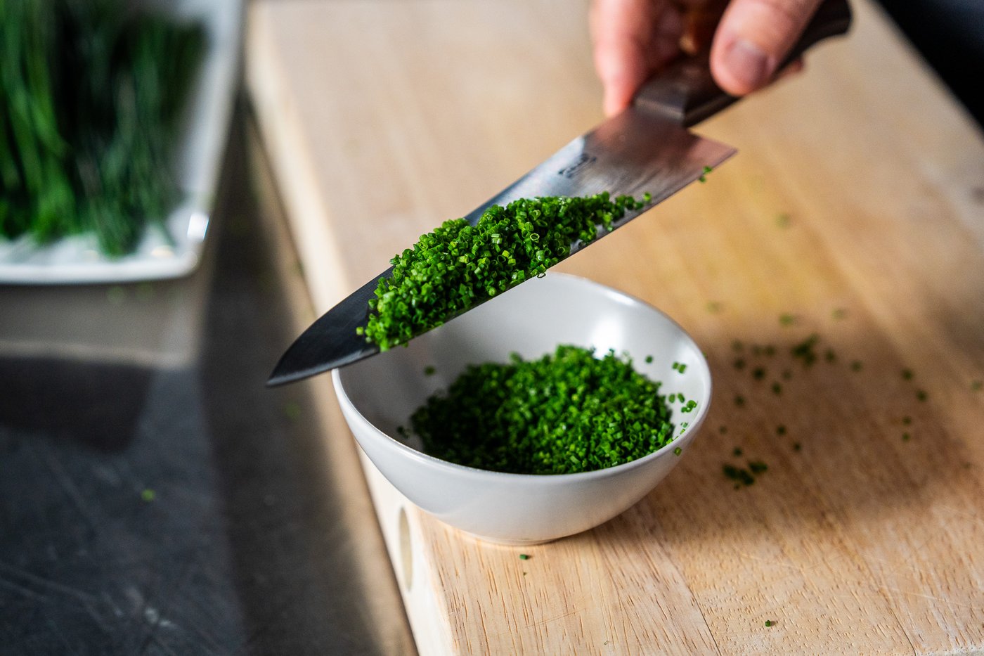 Fint oppkuttet gressløk i en hvit bolle. Gressløk hvile på kniven over bollen.