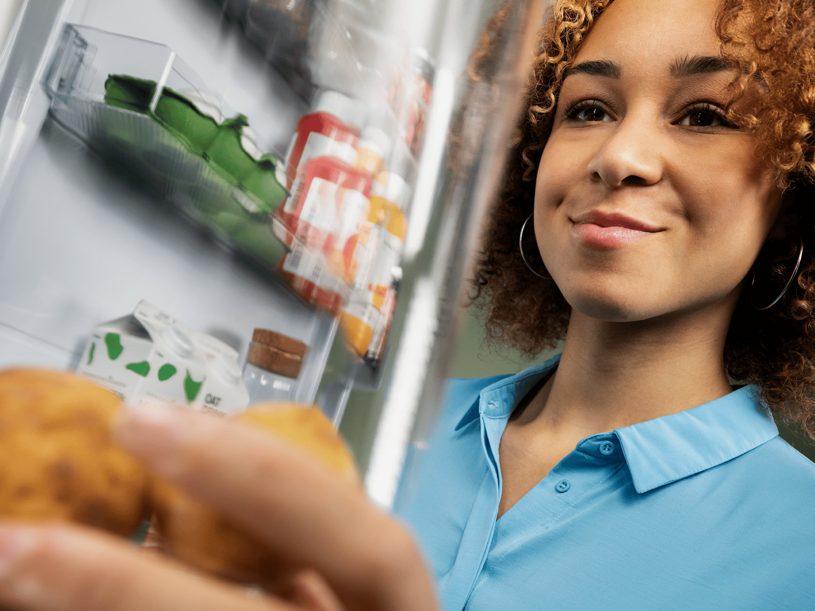 A person is smiling while reaching into a refrigerator to pick up something up.