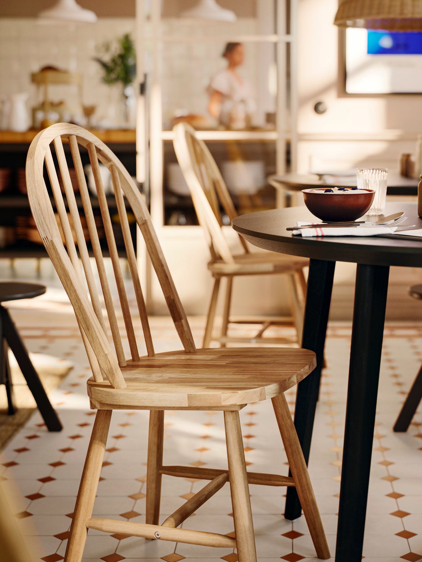 A solid acacia SKOGSTA chair with an arched backrest and spindles is at a dark, round table in a commercial dining area.