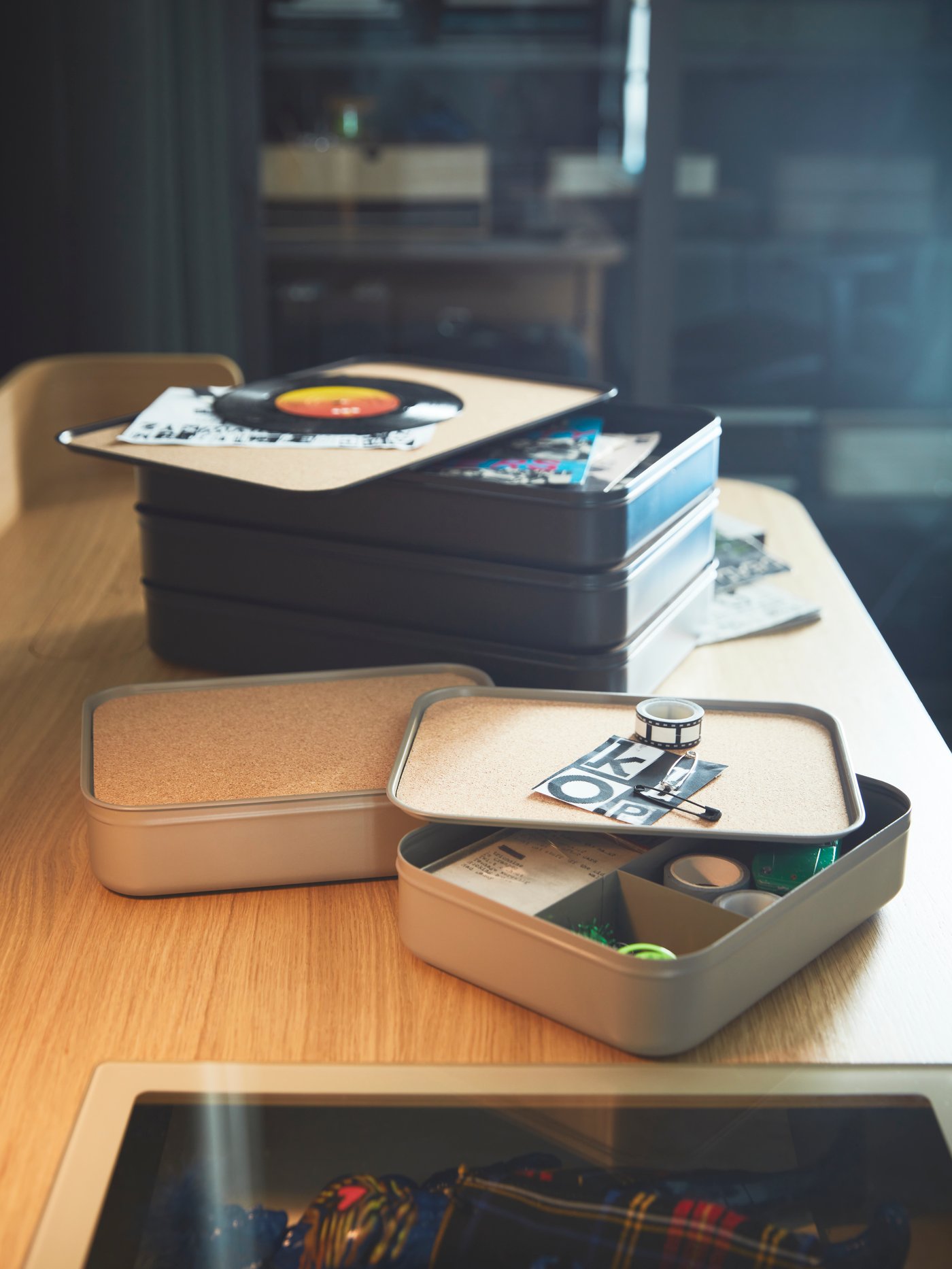 Multiple HARVMATTA boxes of two different kinds stacke and spread on the wooden desktop of a RIDSPÖ desk.
