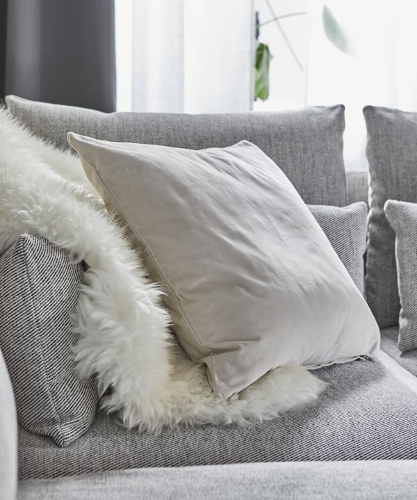 Ein SANELA Kissen liegt auf einem grauen Sofa.