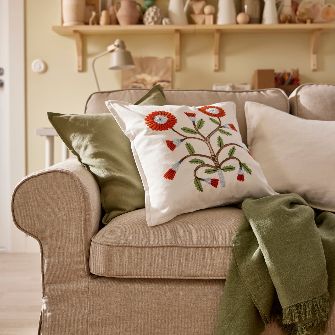 A DYTÅG throw and three cushions, including one with a flowery FACELIOR cushion cover, lie on an EKTORP sofa.
