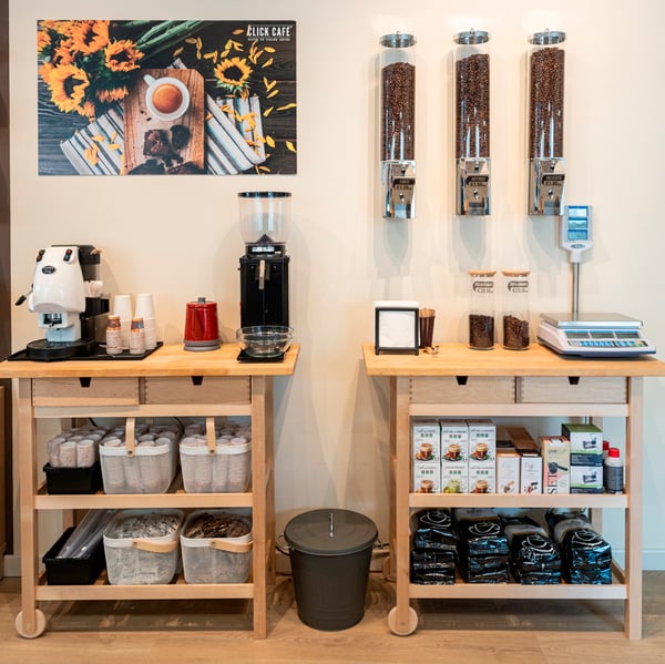 Interno di un Click Cafè con due carrelli FÖRHÖJA. Sui carrelli ci sono contenitori RISATORP contenenti zucchero e palettine, macchine da caffè, una bilancia, barattoli e dispenser con chicchi di caffè. Tra i due carrelli c'è un bidone KNODD.