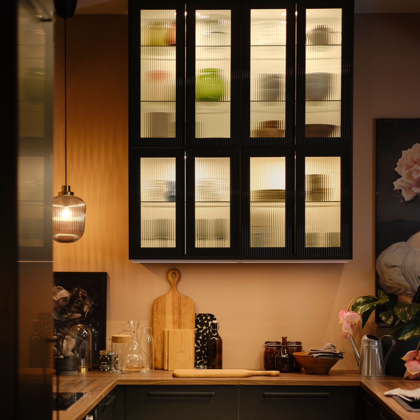 White METOD wall cabinets with shelves and anthracite HEJSTA reeded glass doors with various items and lighting inside.