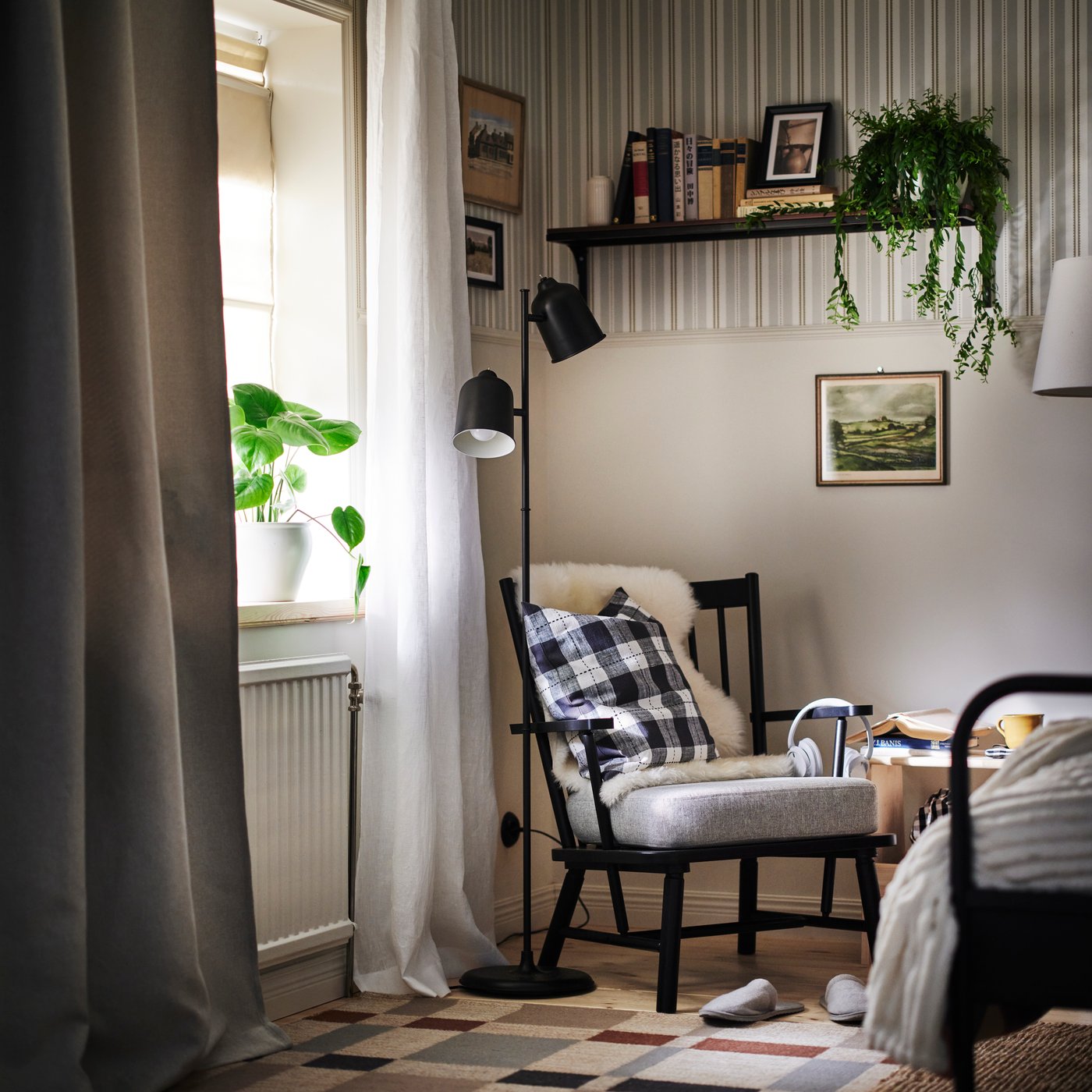 Een hoek van een slaapkamer met de PERSBOL fauteuil en de KLÖVING staande lamp in zwart. Het raam zit links en het bed staat rechts.