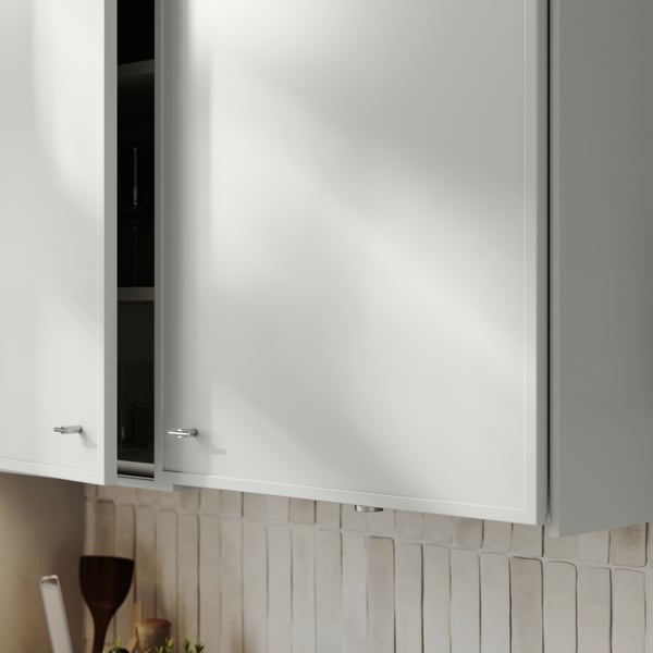 Ett köksskåp med ASPUDDEN-dörrar i ljusgrått, något öppna, med dricksglas och vinglas inuti.