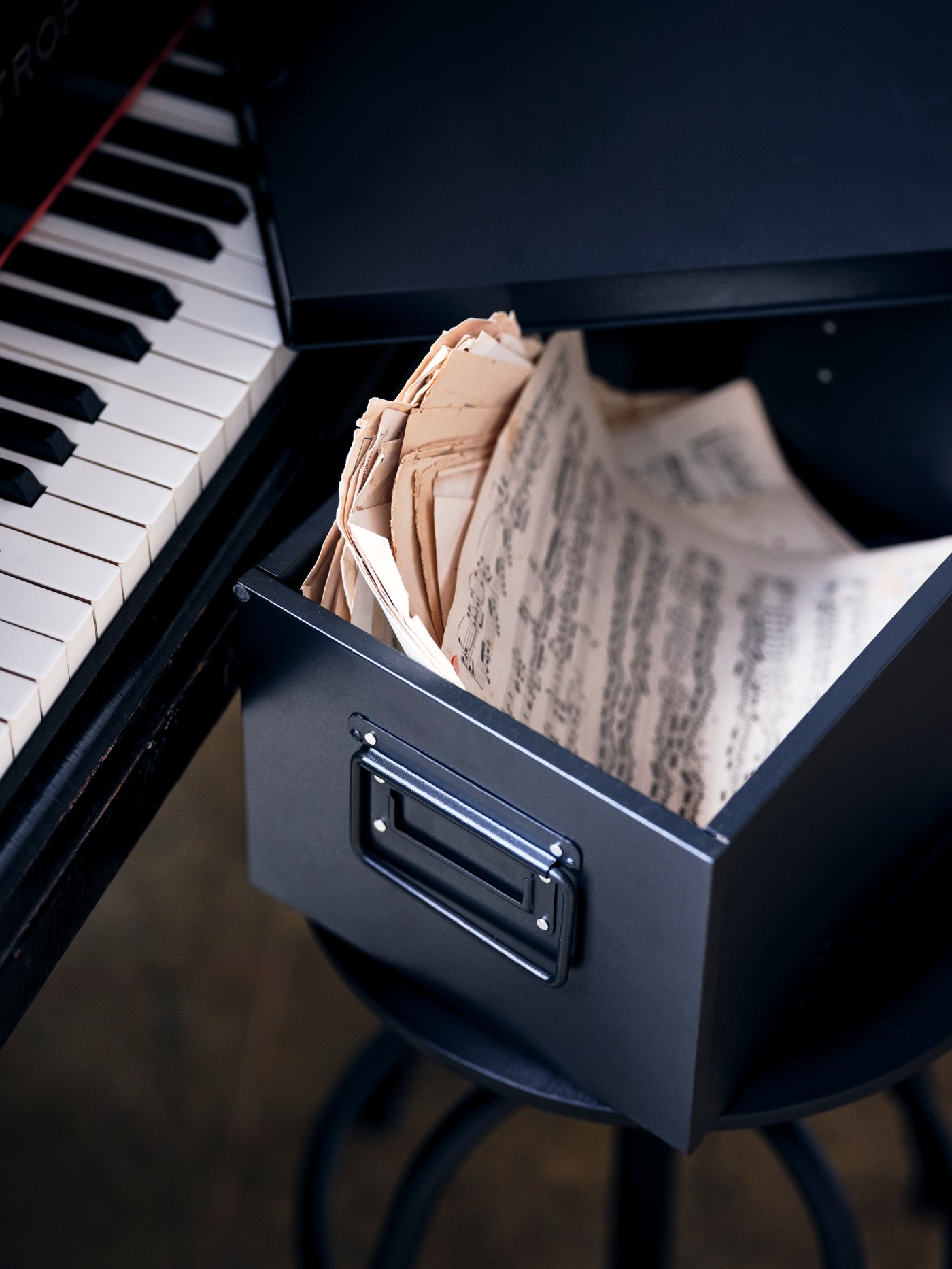 صندوق تخزين MANICK مملوء بورق ملاحظات، على مقعد أمام بيانو.