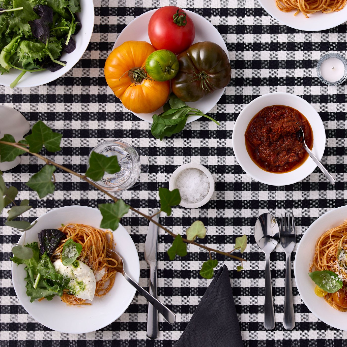 White plates and bowls from the OFTAST series are filled with food and placed on a black and white checkered tablecloth.