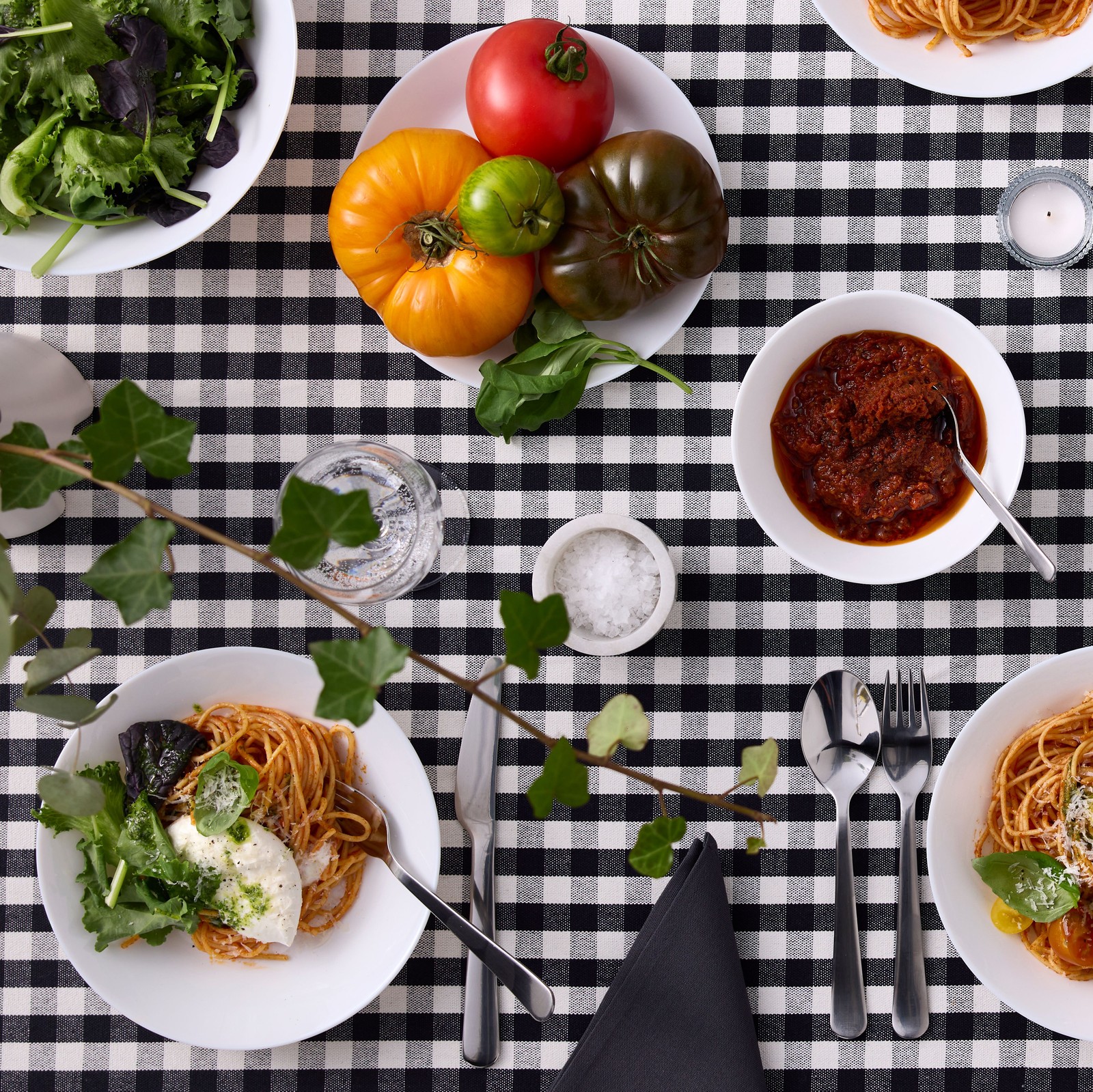 Varios pratos e cuncos OFTAST brancos cheos de comida e colocados sobre un mantel de cadros brancos e negros.