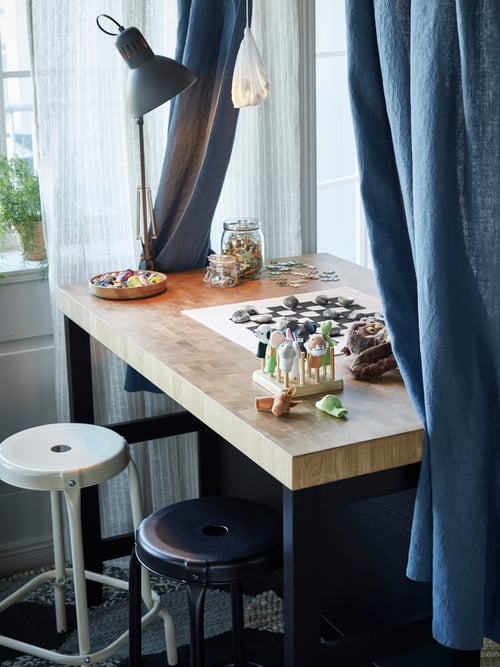A modern kitchen featuring a kitchen island with a rack, two bar stools, a pair of curtains, and a work lamp.