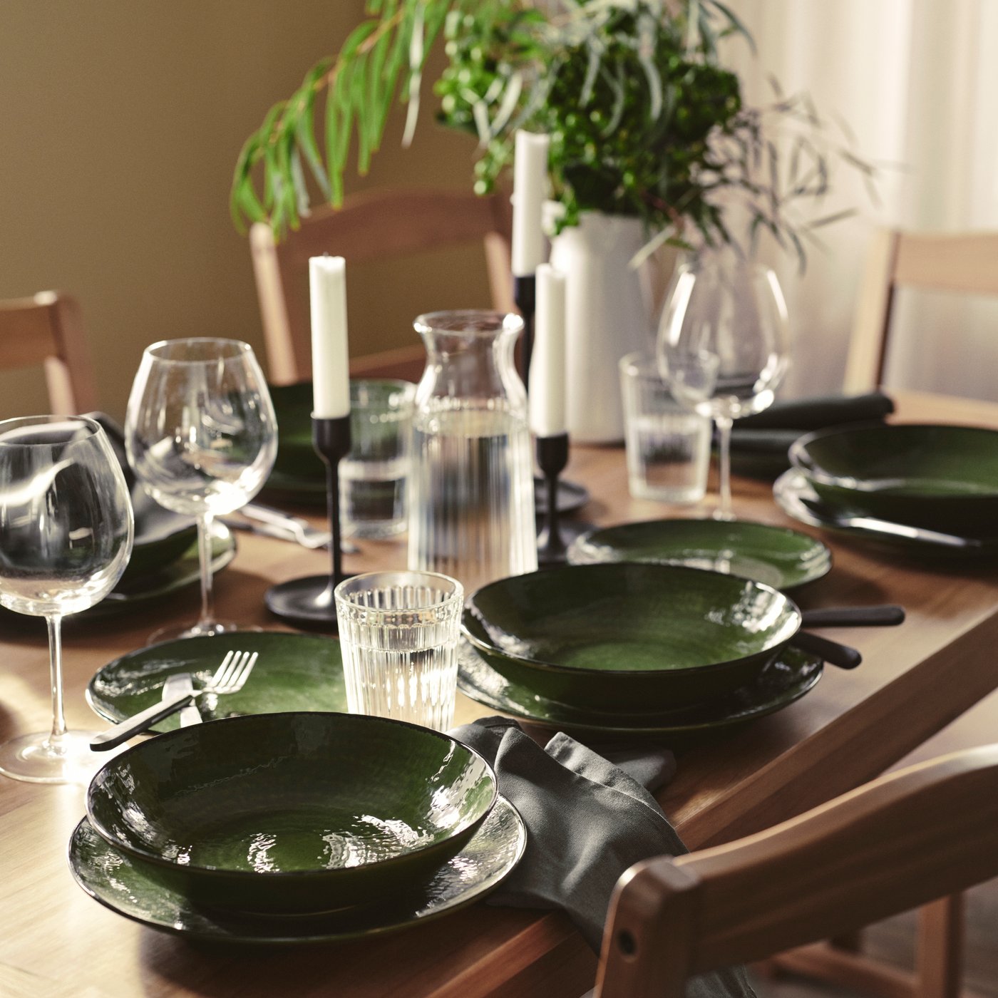 Green dinnerware placed on table, with glasses and cutlery.