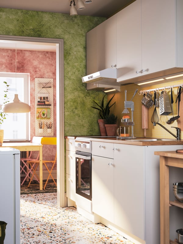 A white KNOXHULT kitchen with base and wall cabinets, facing a fridge. A dining area can be seen the background.