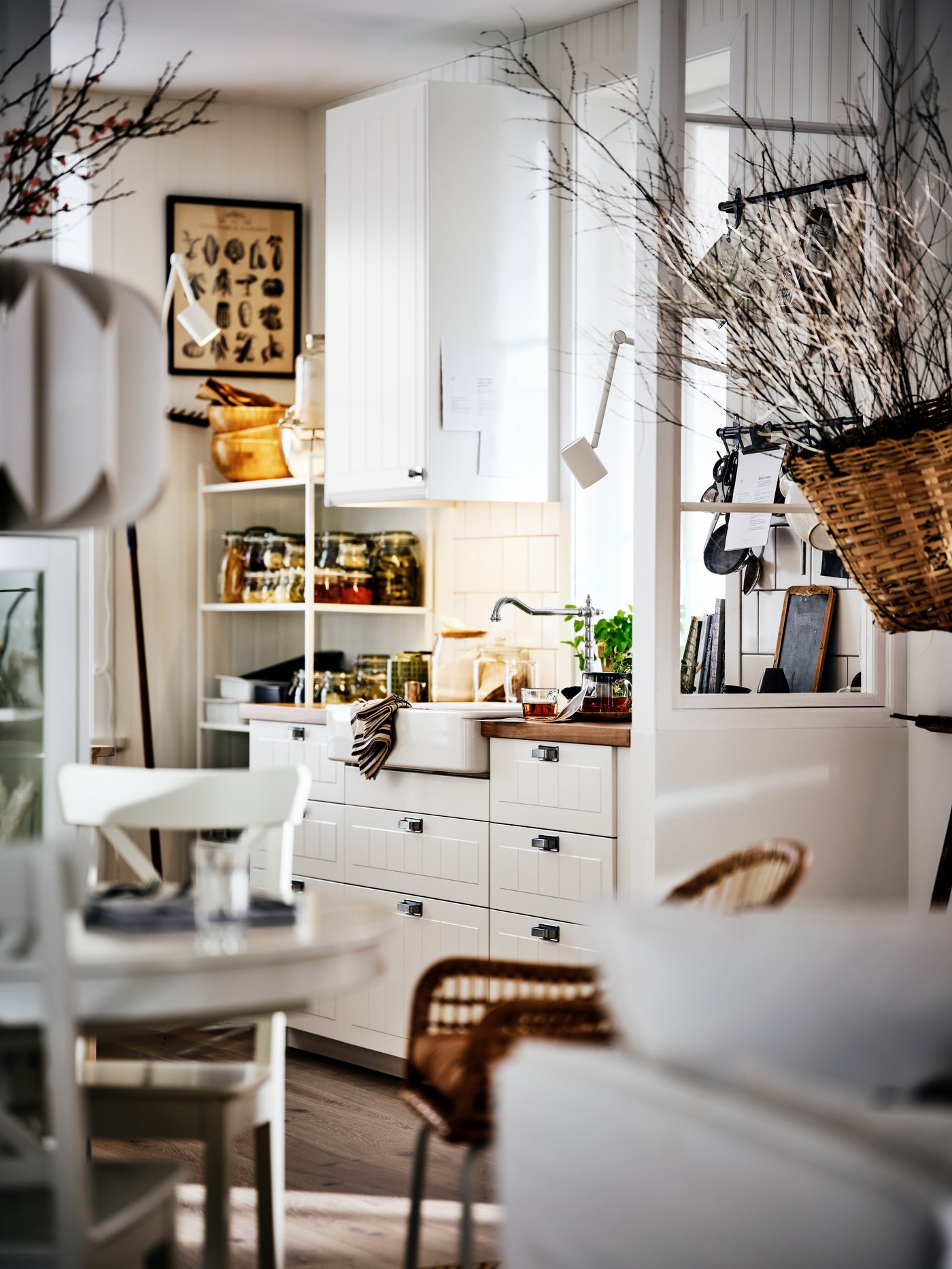 A country-style kitchen and dining area, with white cabinets, a round table and chairs and open shelves holding food jars.