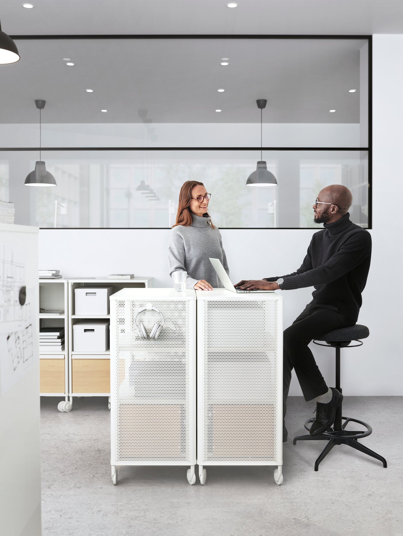 גבר ואישה משוחחים במשרד לצד יחידת אחסון לבנה. מאחוריהם, על התקרה תלויות מנורות.