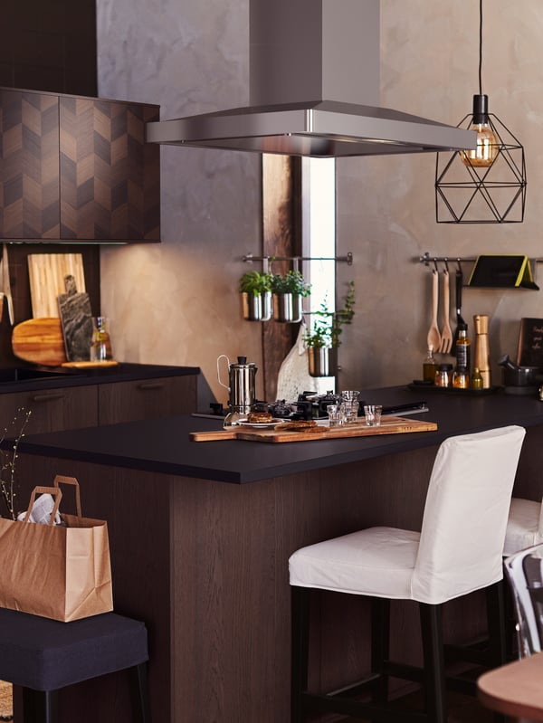 Dapur dengan pulau dapur kayu berwarna gelap yang mempunyai lampu pendan BRUNSTA tergantung di atasnya. Teko kopi dan gelas terletak di atas kaunter.
