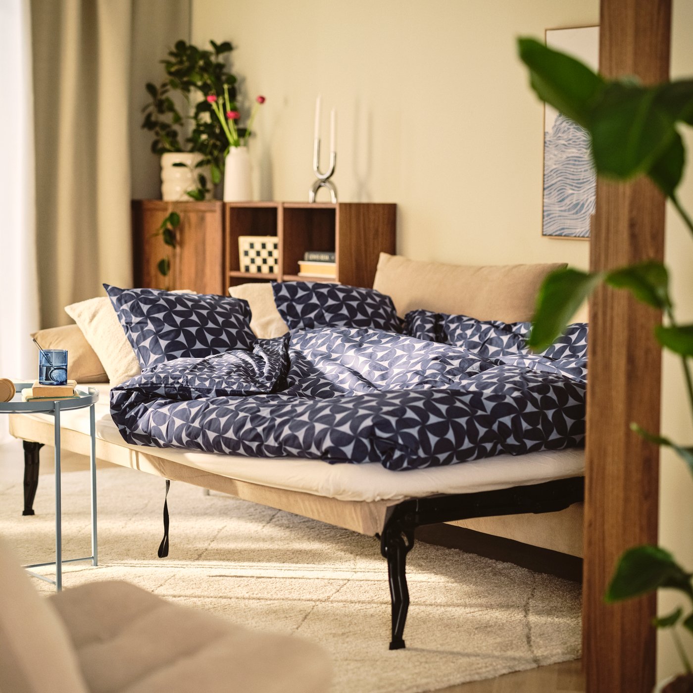 A living room with a beige SÖDERHAMN 3-seat sofa-bed, upholstered in Kelinge beige, surrounded by cushions and plants.