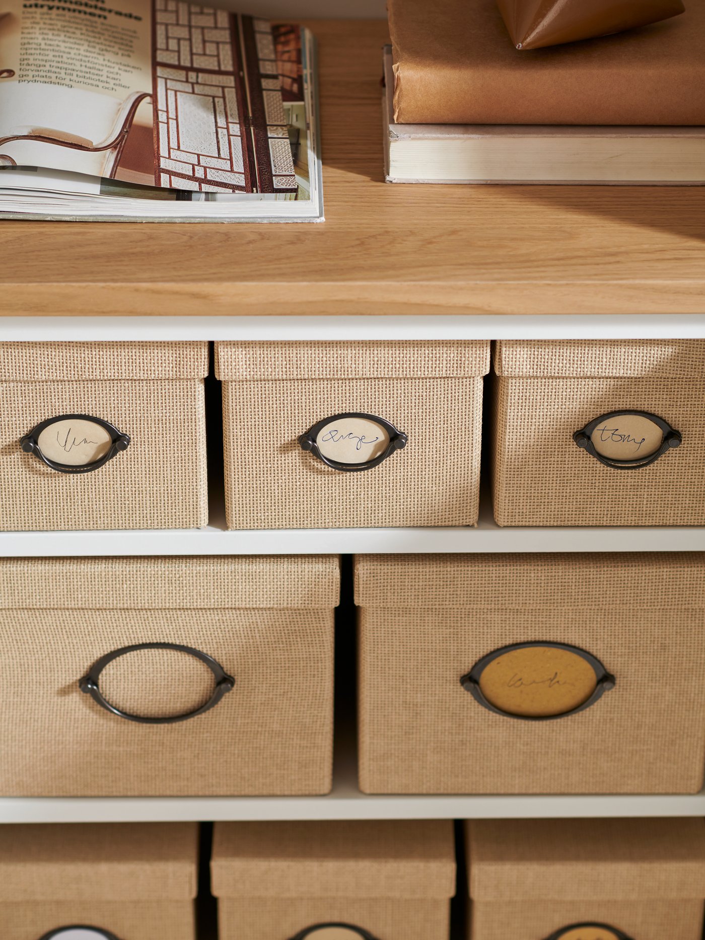 Varias cajas rectangulares con tapa colocadas en estantes blancos. Encima del estante superior hay un panel superior beige.